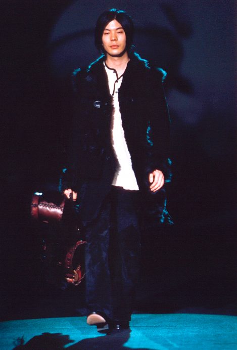 Musician and co-founder of the rock band Smashing Pumpkins James Iha wears a pair of custom-made Lost Art suede pants, walking in the Anna Sui 1999 Fall fashion show, carrying a custom-made Lost Art leather guitar case lined with fur